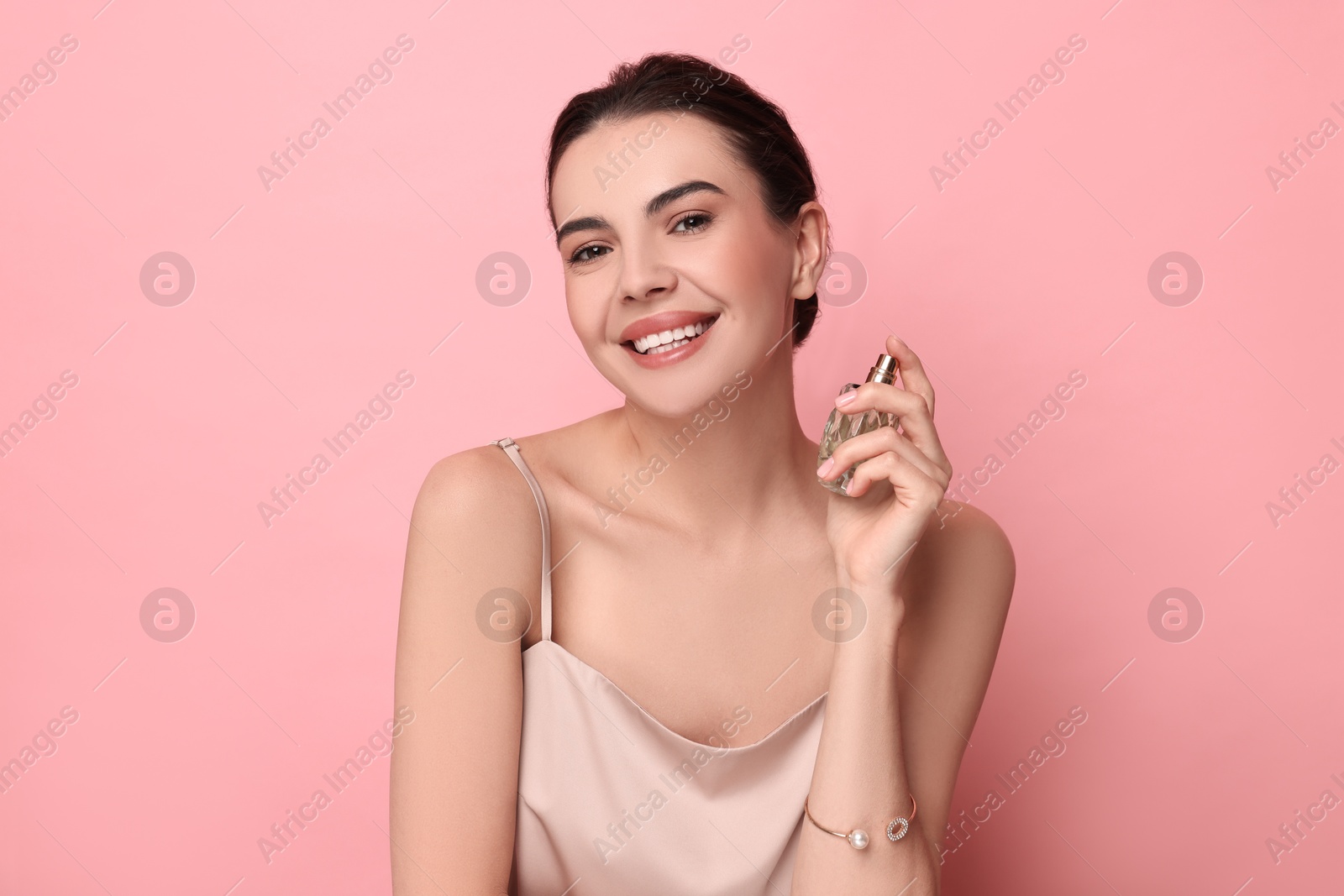 Photo of Smiling woman with bottle of perfume on pink background