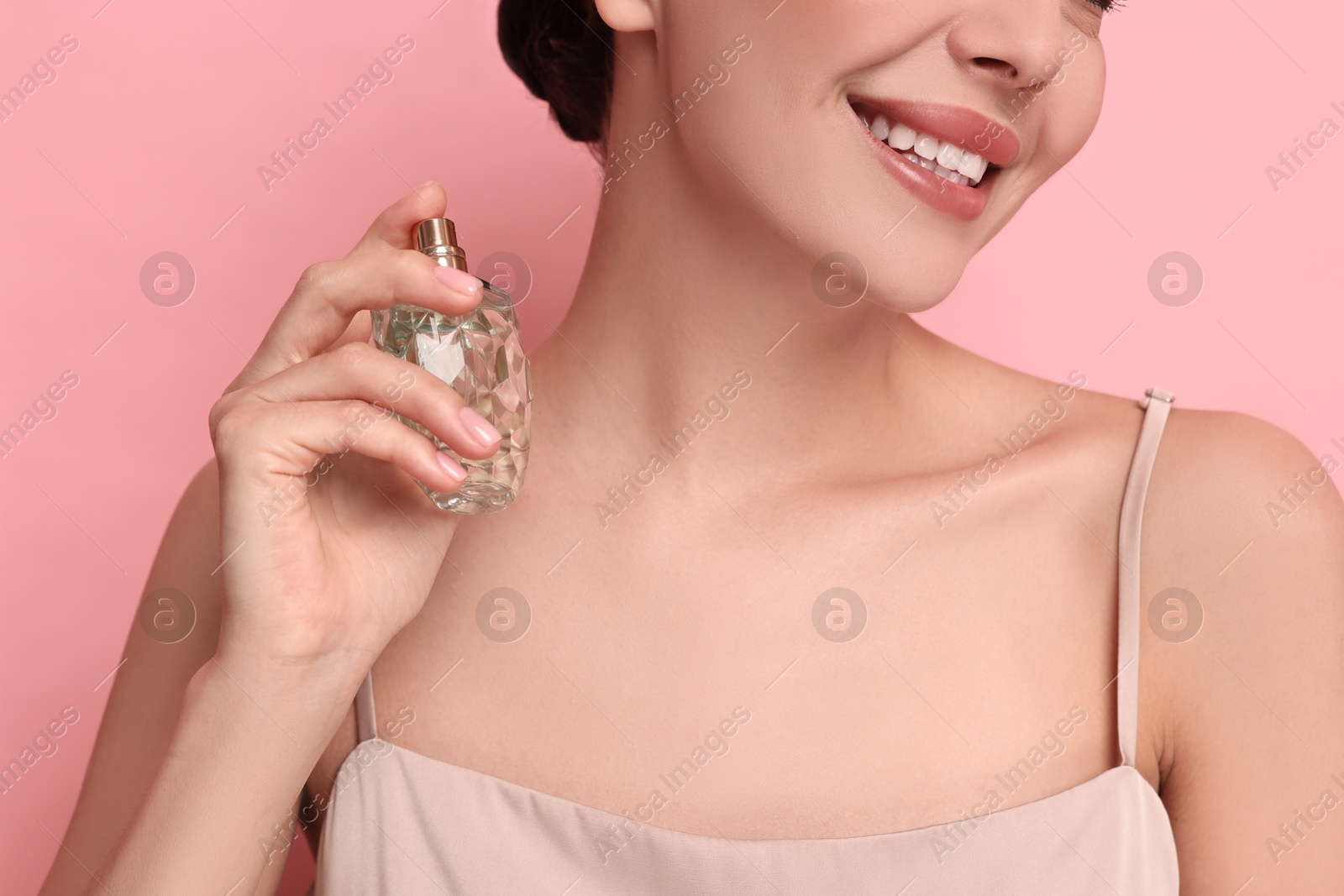 Photo of Smiling woman with bottle of perfume on pink background, closeup