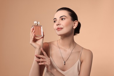 Beautiful woman with bottle of perfume on beige background