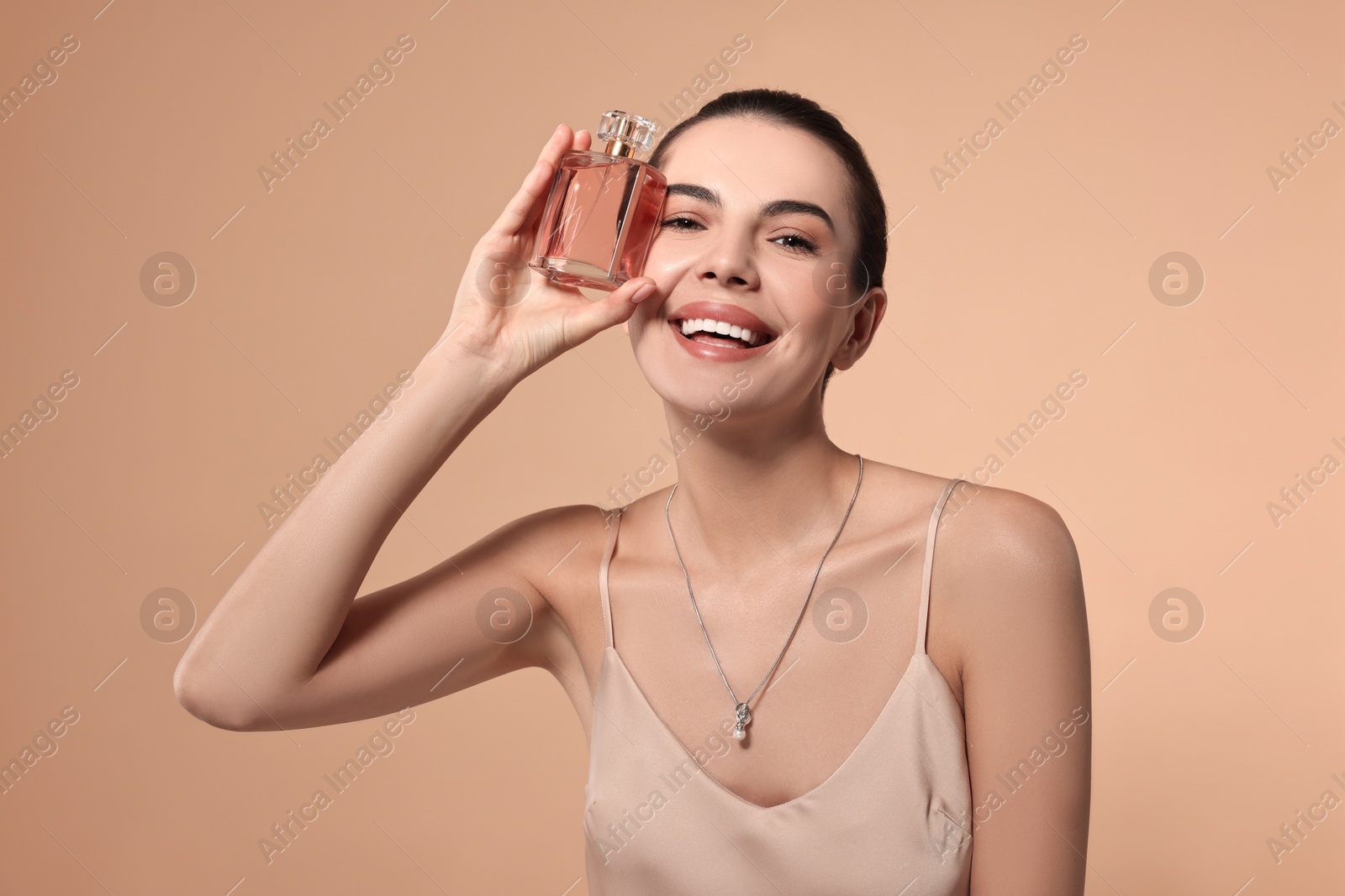 Photo of Happy woman with bottle of perfume on beige background