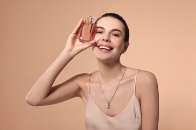 Happy woman with bottle of perfume on beige background