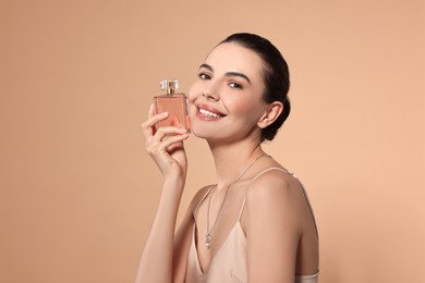 Smiling woman with bottle of perfume on beige background