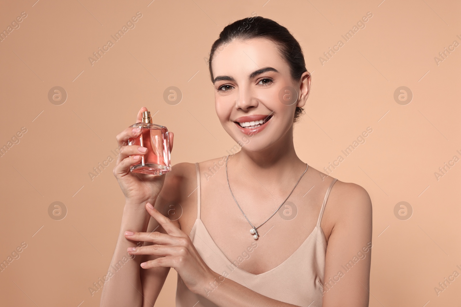 Photo of Smiling woman with bottle of perfume on beige background