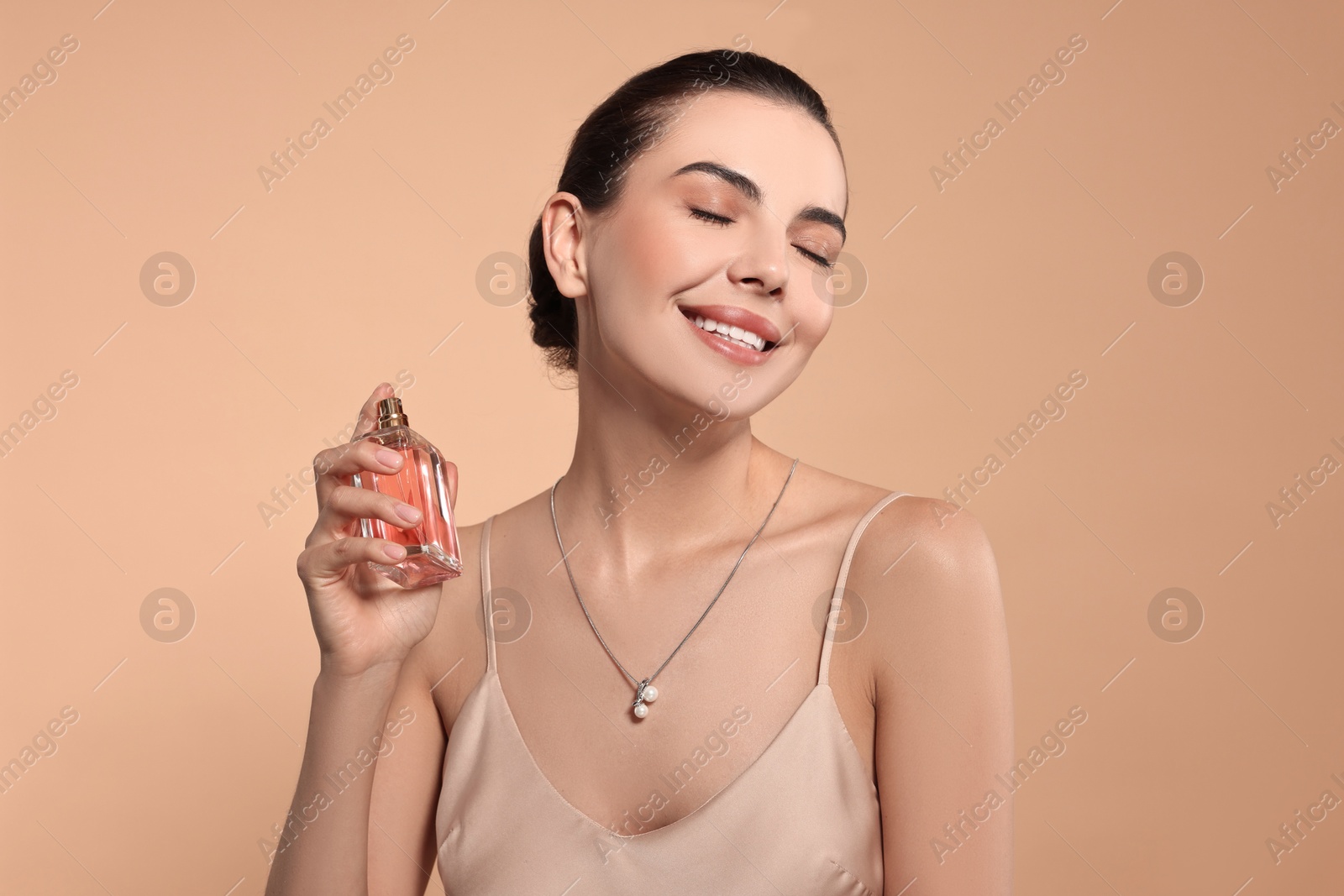 Photo of Smiling woman with bottle of perfume on beige background