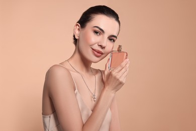 Beautiful woman with bottle of perfume on beige background