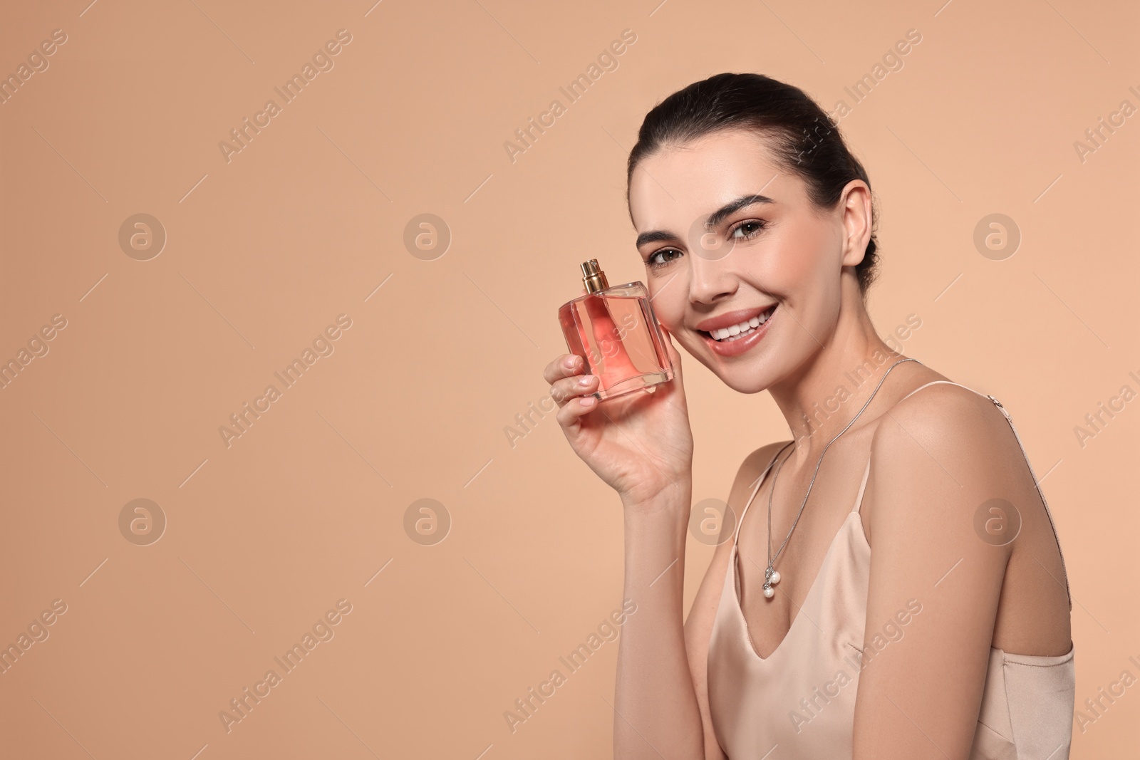 Photo of Smiling woman with bottle of perfume on beige background. Space for text