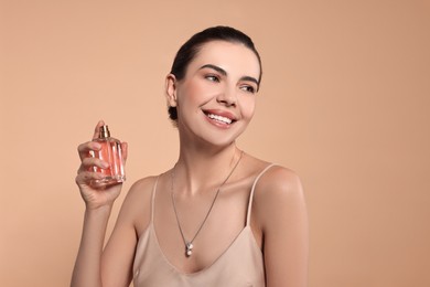 Photo of Smiling woman with bottle of perfume on beige background