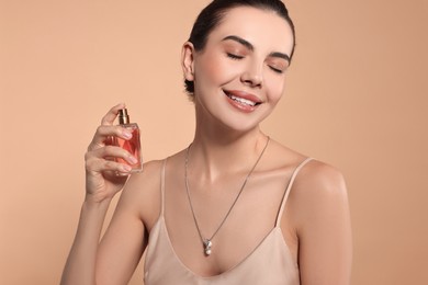 Photo of Smiling woman with bottle of perfume on beige background