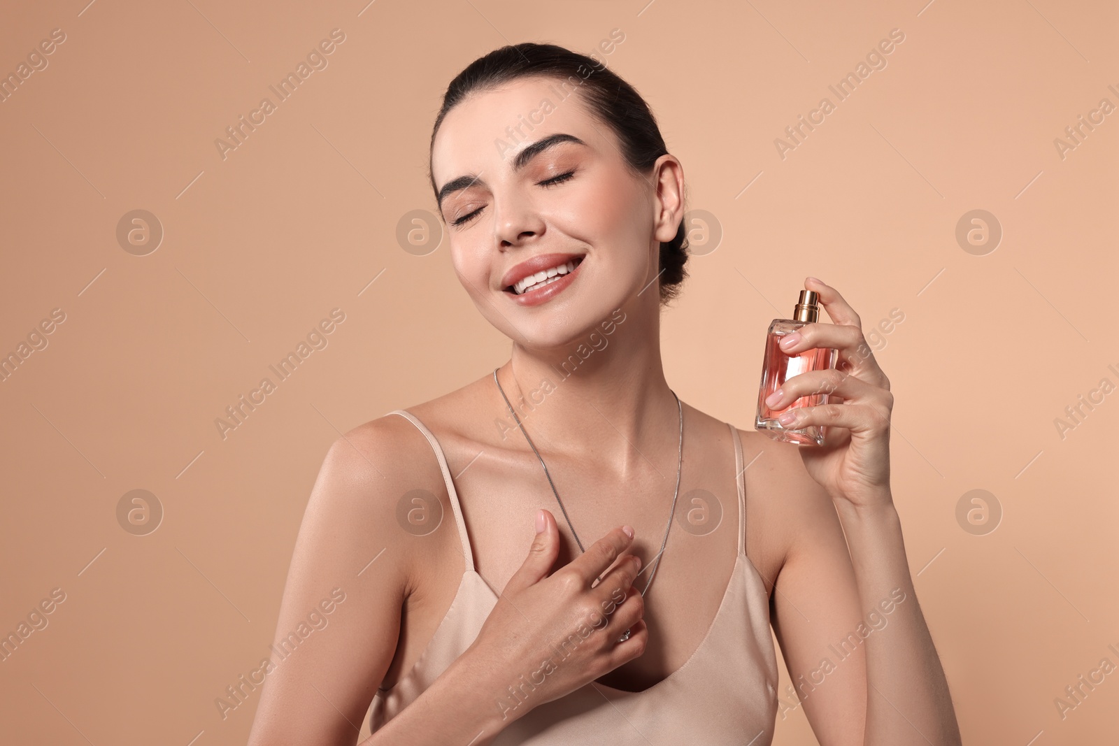 Photo of Smiling woman with bottle of perfume on beige background