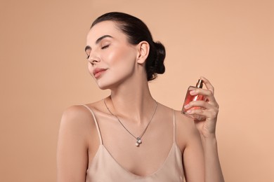 Beautiful woman spraying perfume on beige background