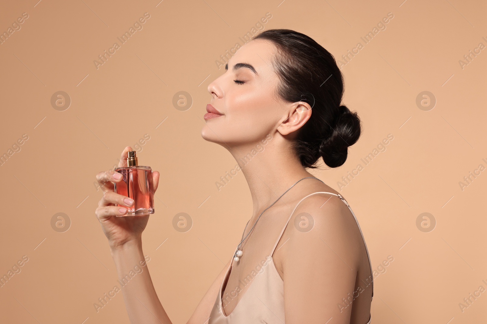 Photo of Beautiful woman spraying perfume on beige background