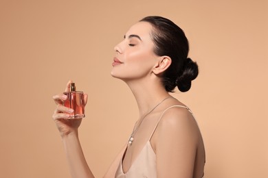 Beautiful woman spraying perfume on beige background