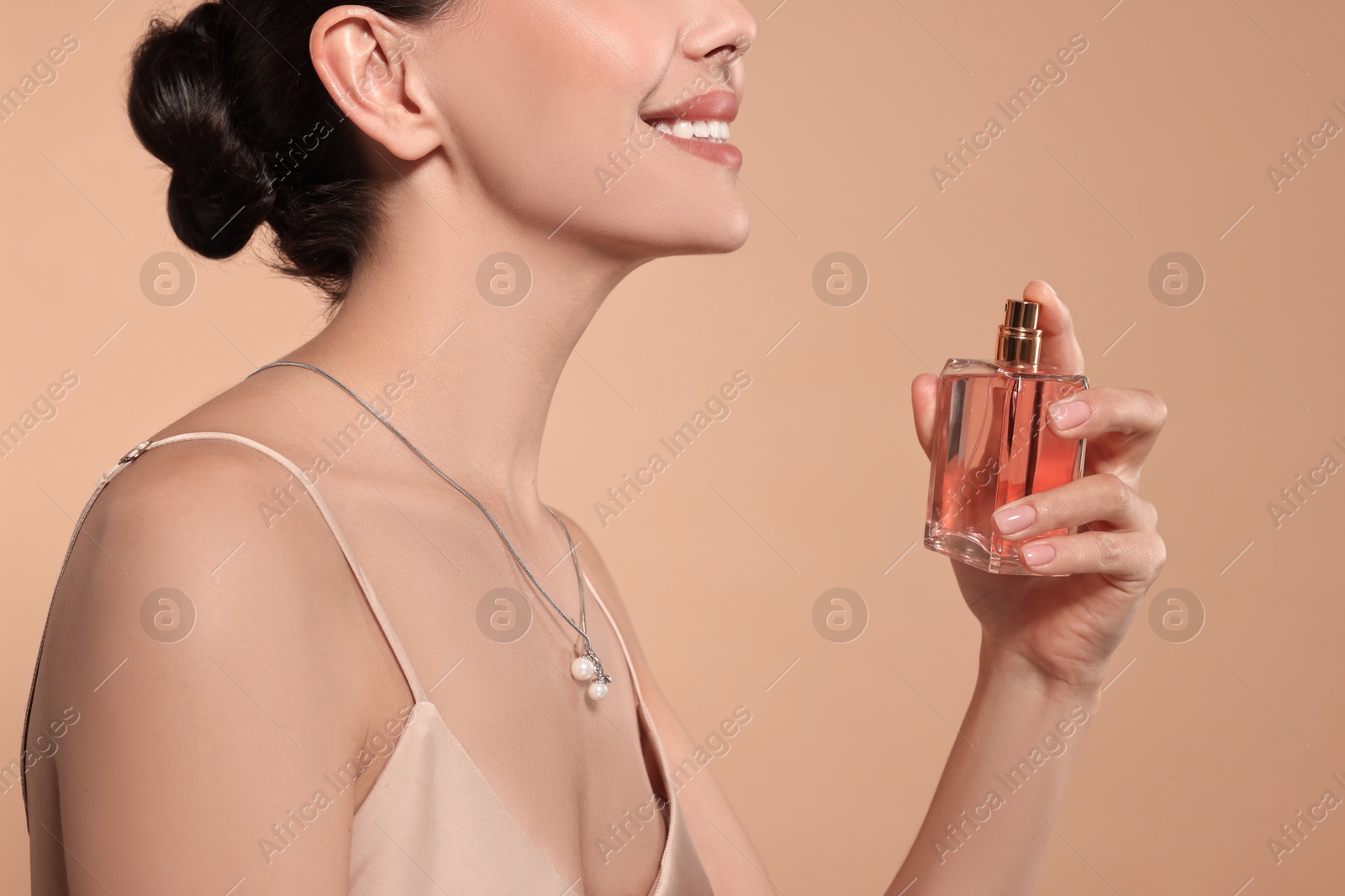 Photo of Smiling woman spraying perfume on beige background, closeup