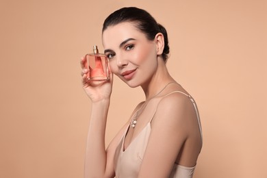 Beautiful woman with bottle of perfume on beige background