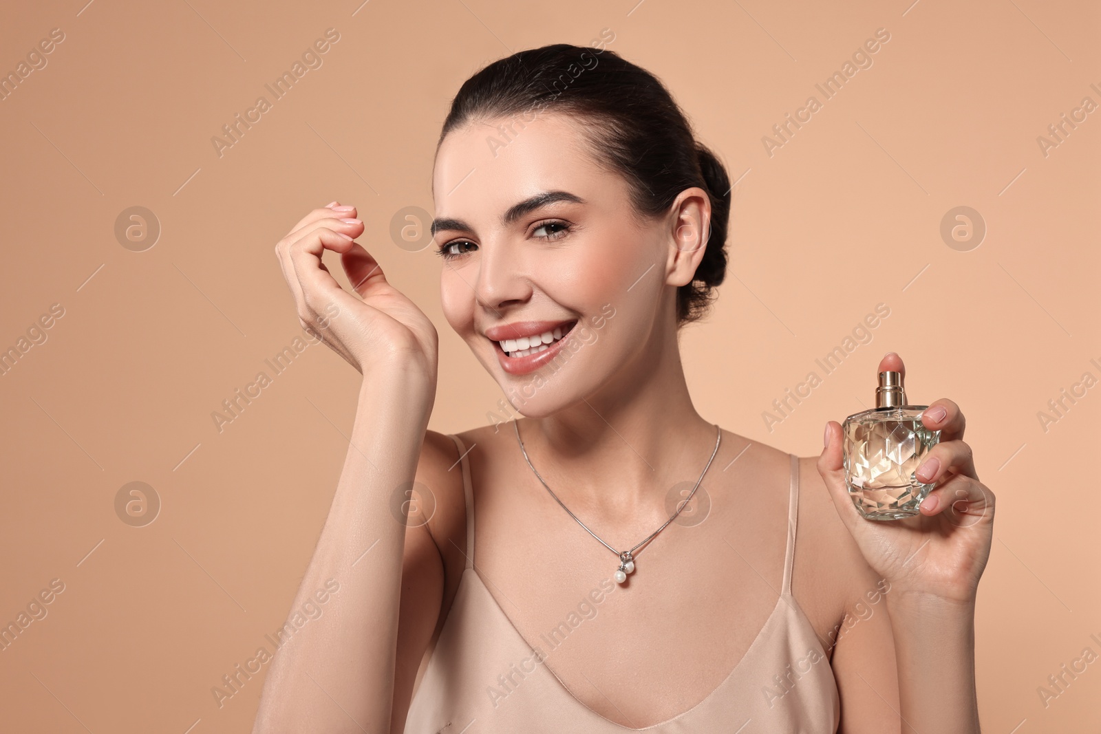 Photo of Smiling woman smelling perfume on wrist against beige background