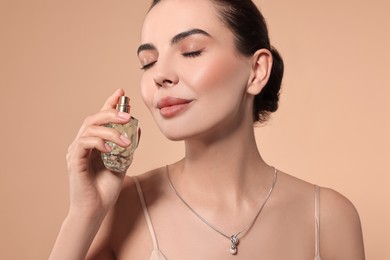 Beautiful woman with bottle of perfume on beige background