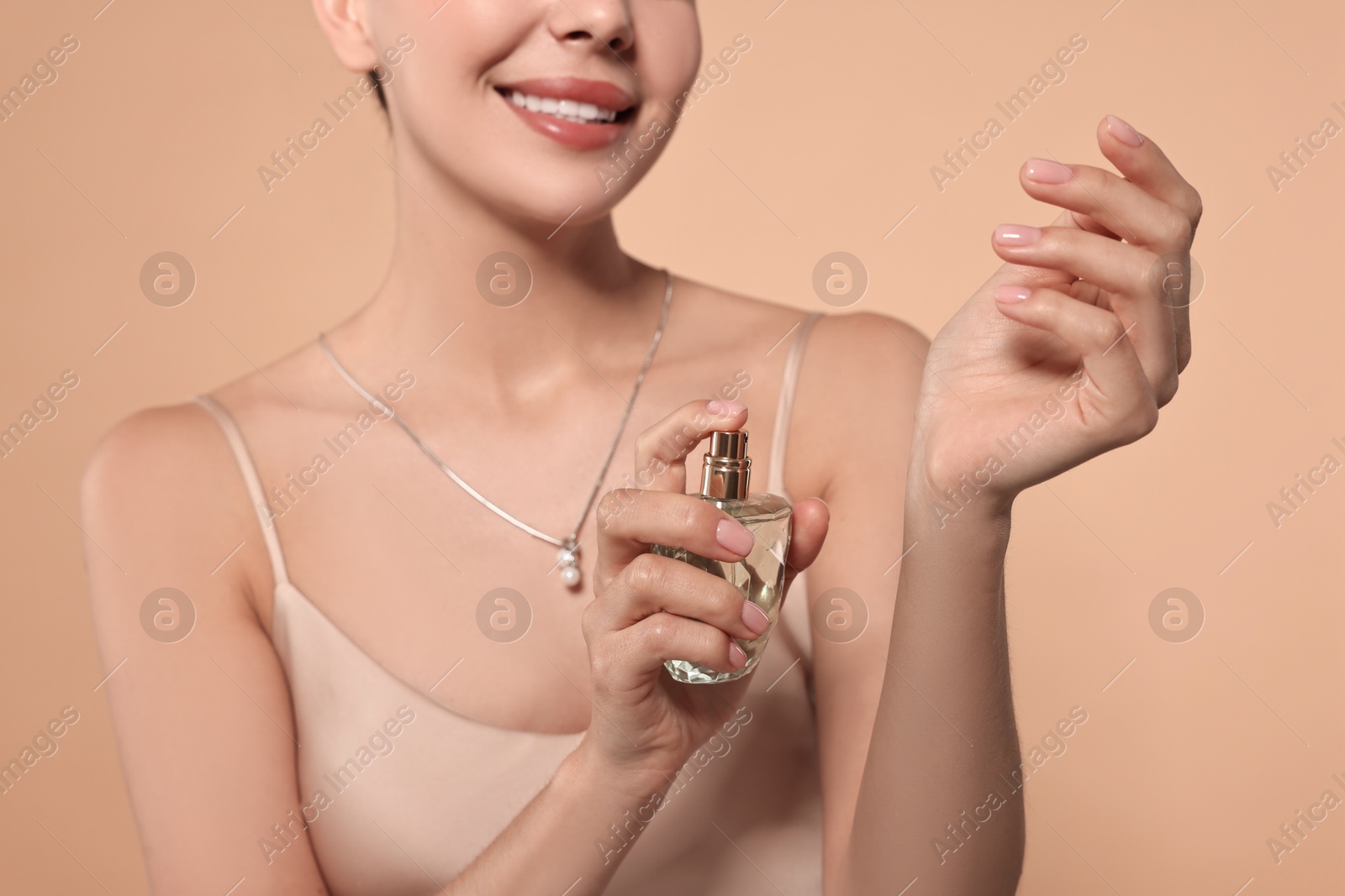 Photo of Smiling woman spraying perfume onto wrist against beige background, closeup