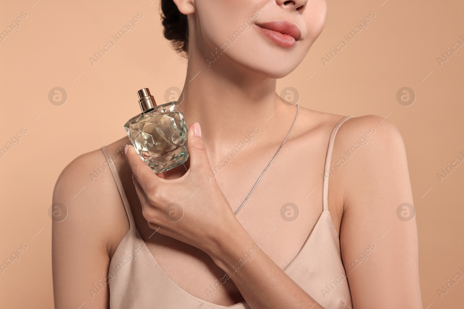 Photo of Woman with bottle of perfume on beige background, closeup