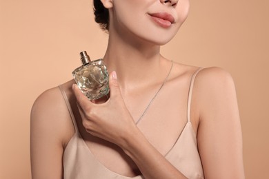 Woman with bottle of perfume on beige background, closeup