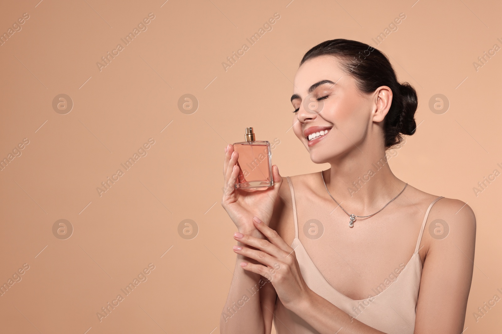 Photo of Smiling woman with bottle of perfume on beige background. Space for text