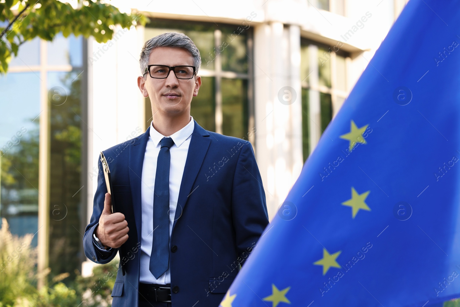 Photo of International relations. Diplomat with clipboard near flag of European Union outdoors