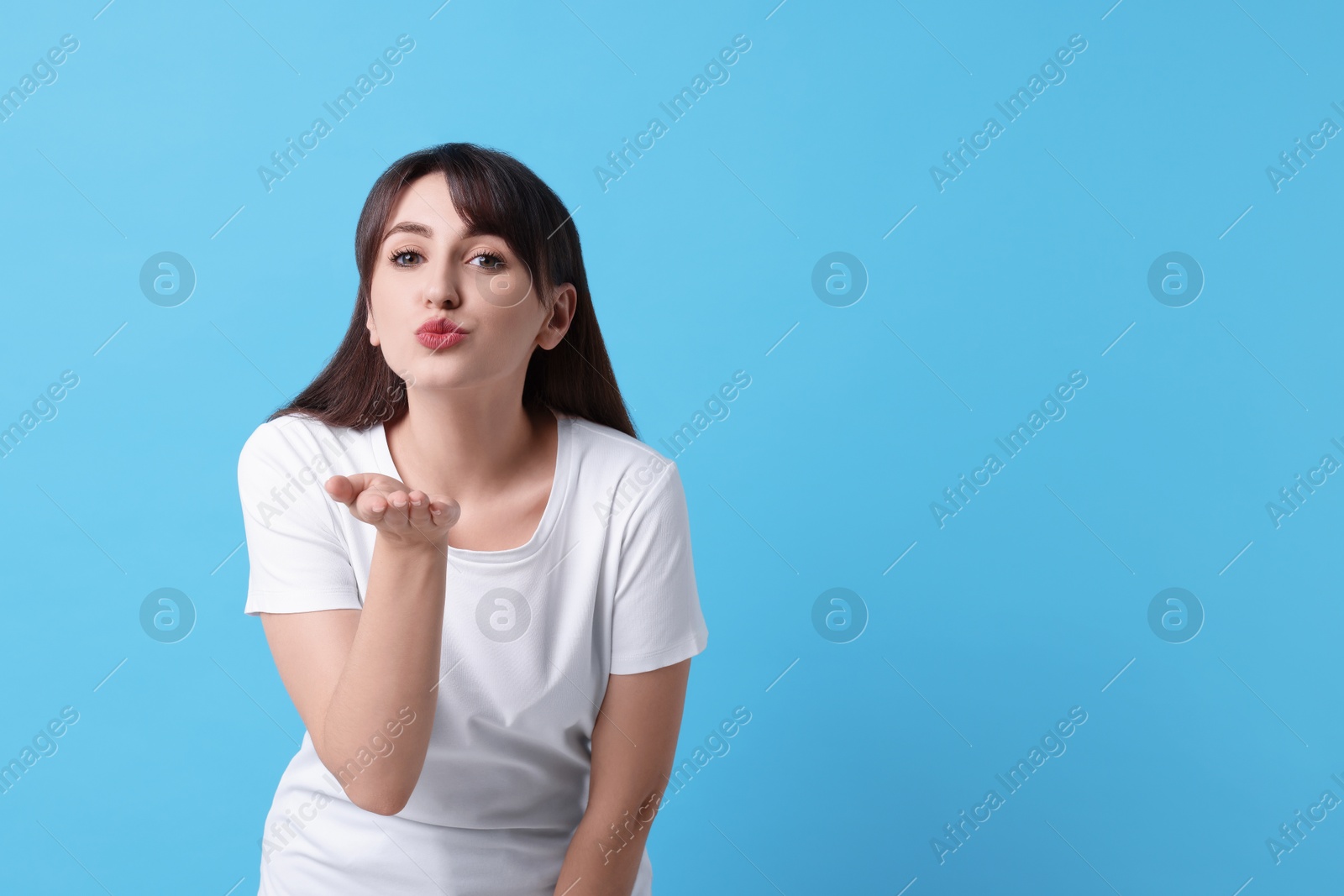 Photo of Beautiful woman blowing kiss on light blue background, space for text