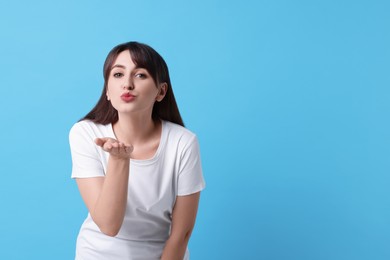 Beautiful woman blowing kiss on light blue background, space for text