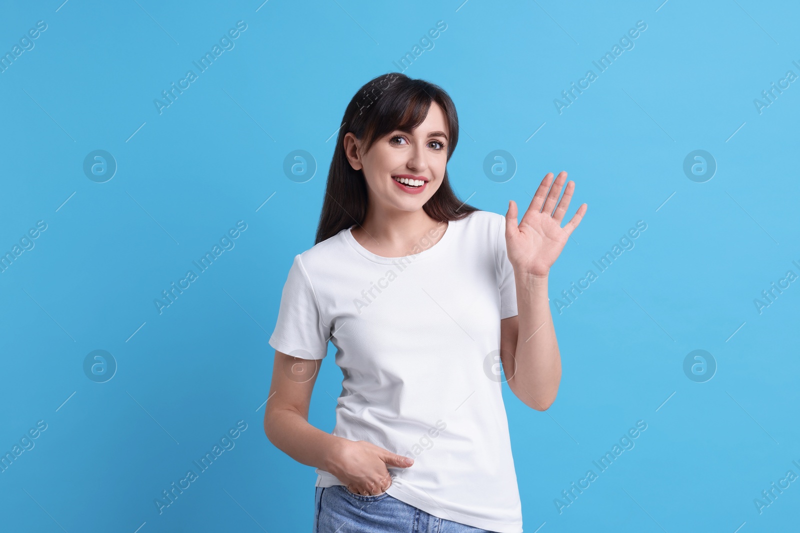 Photo of Happy woman waving on light blue background