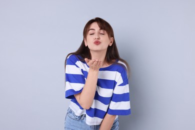 Beautiful woman blowing kiss on light grey background