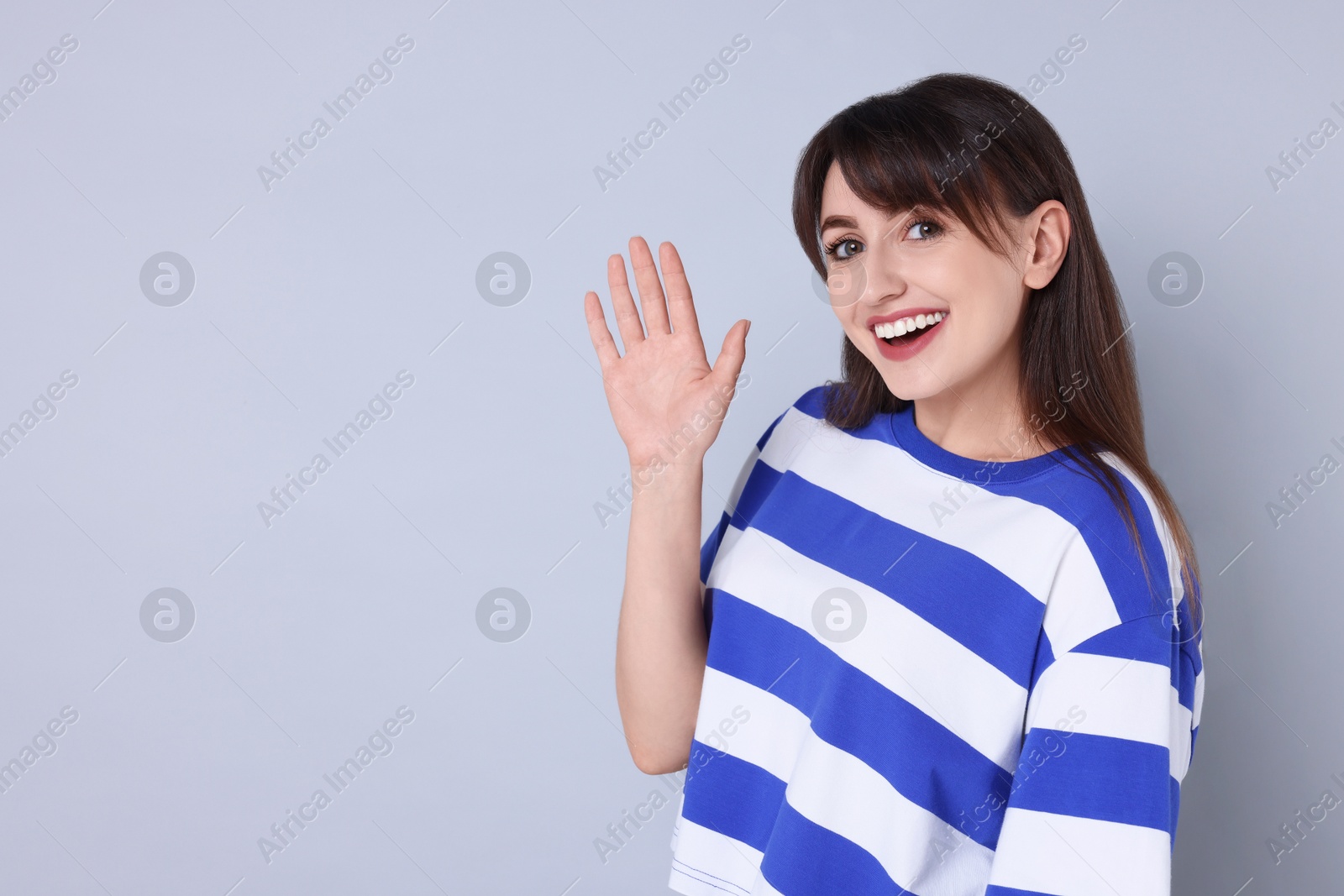 Photo of Happy woman waving on light grey background, space for text