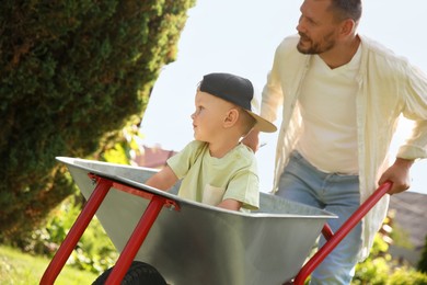 Father pushing wheelbarrow with his son outdoors, selective focus