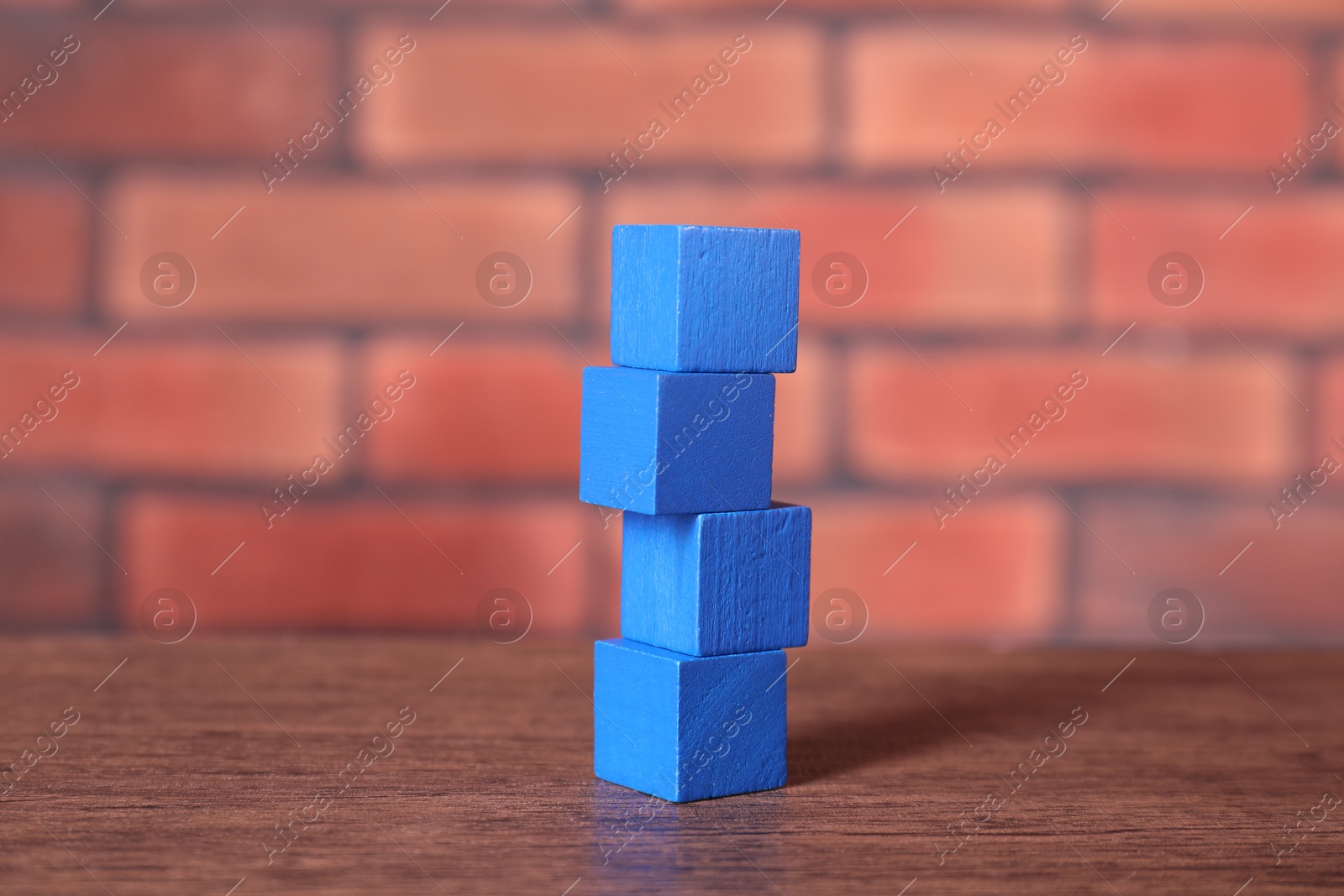 Photo of Blank colorful cubes on wooden table against brick wall