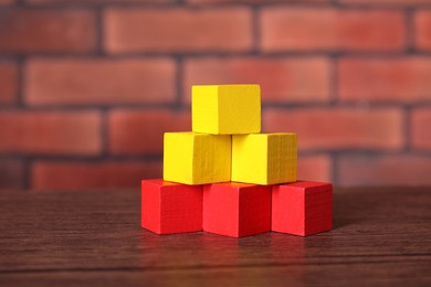 Photo of Blank colorful cubes on wooden table against brick wall