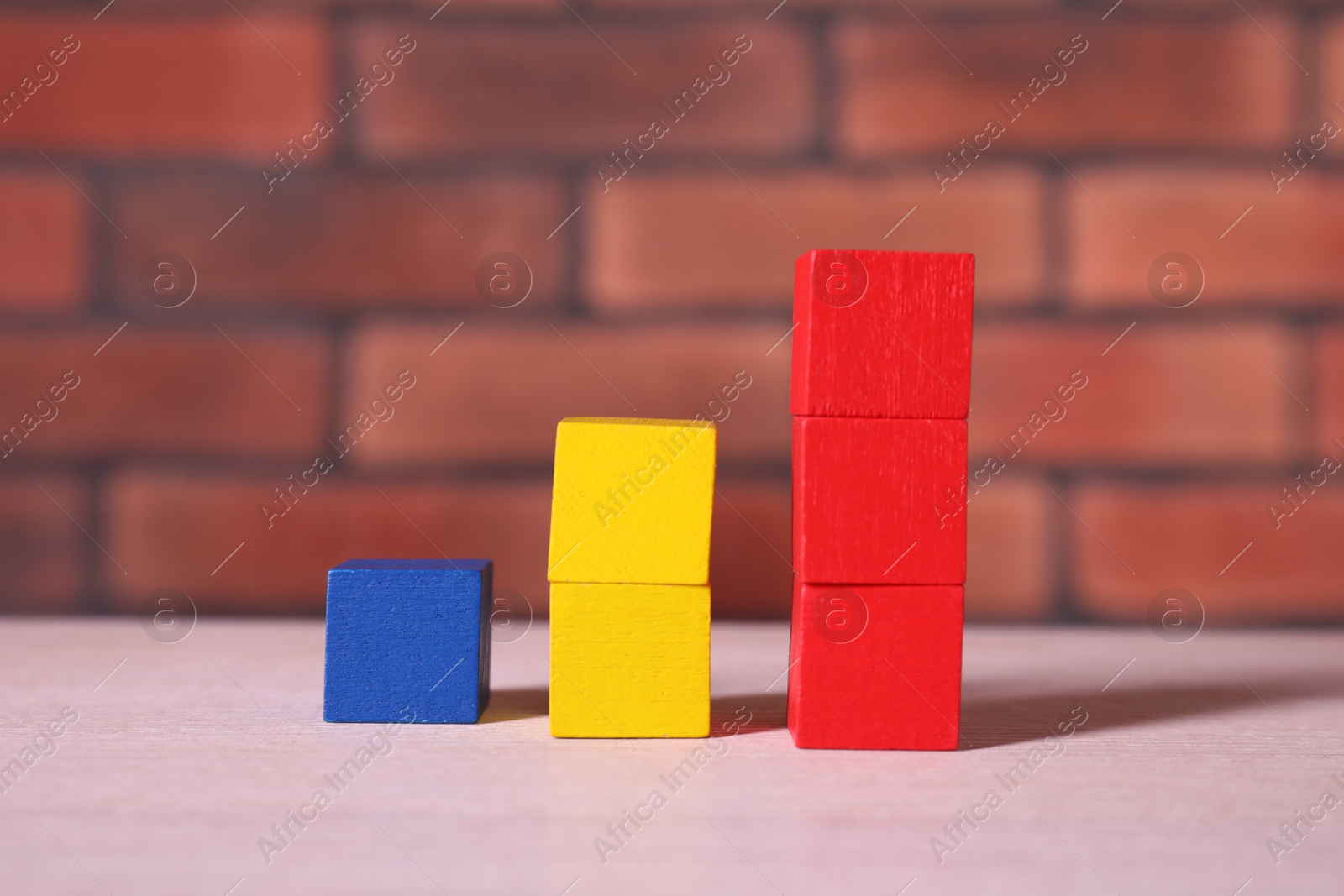 Photo of Blank colorful cubes on wooden table against brick wall