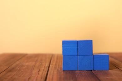 Photo of Blank colorful cubes on wooden table against pale yellow background, space for text