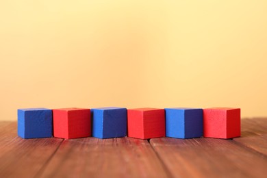 Photo of Blank colorful cubes on wooden table against pale yellow background