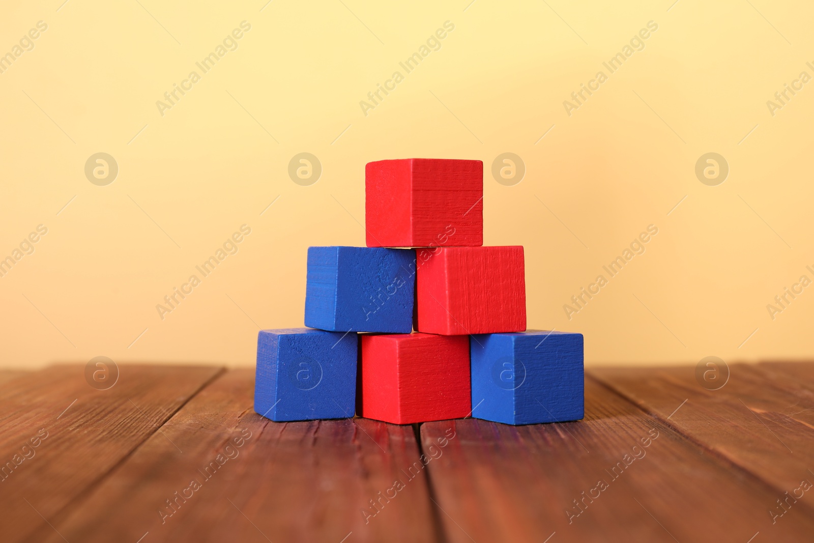 Photo of Blank colorful cubes on wooden table against pale yellow background