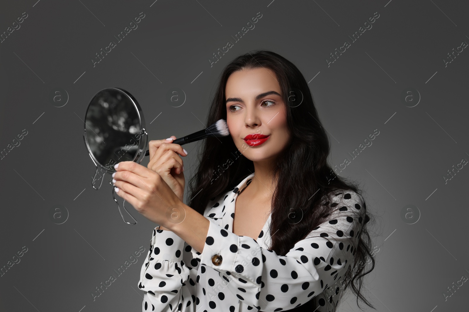 Photo of Beautiful woman with mirror applying makeup on grey background