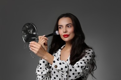 Photo of Beautiful woman with mirror applying makeup on grey background