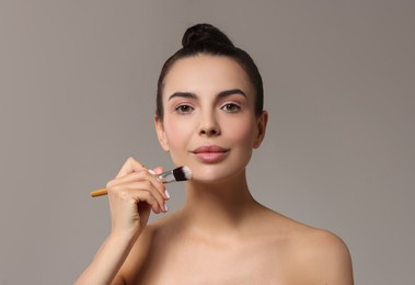 Photo of Beautiful woman applying makeup with brush on grey background