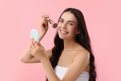 Photo of Beautiful makeup. Smiling woman applying blush with brush on pink background