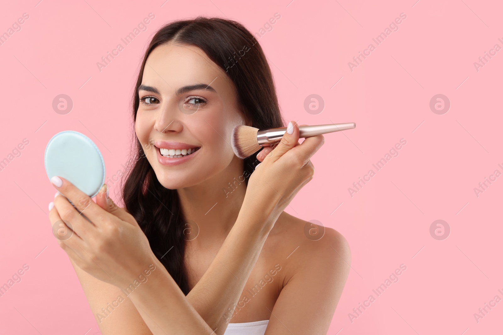 Photo of Beautiful makeup. Smiling woman applying blush with brush on pink background, space for text