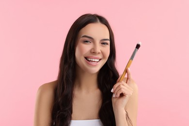 Beautiful makeup. Smiling woman with brush on pink background