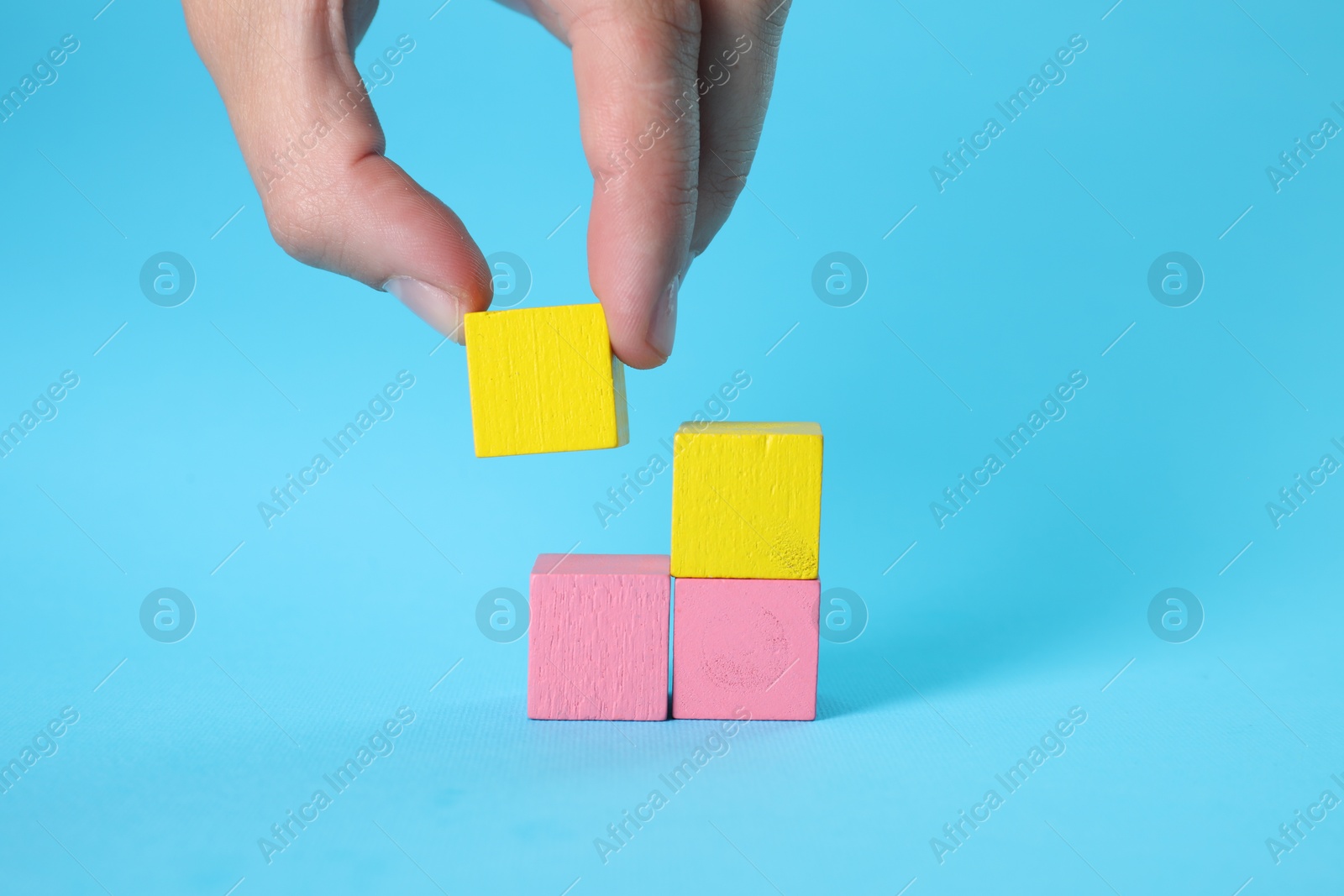 Photo of Woman putting colorful cube to other ones on light blue background, closeup