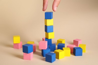 Photo of Woman putting colorful cube to other ones on beige background, closeup