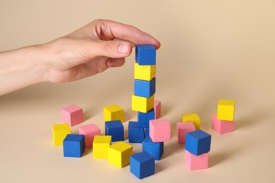 Photo of Woman putting colorful cube to other ones on beige background, closeup