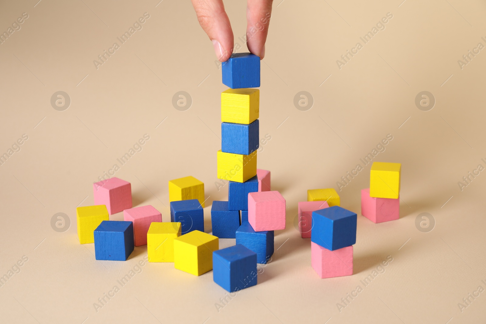 Photo of Woman putting colorful cube to other ones on beige background, closeup