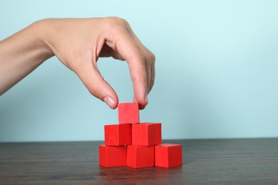 Photo of Woman building pyramid of red cubes at wooden table, closeup