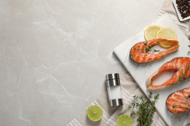 Photo of Tasty grilled salmon steaks, lemon, lime and spices on gray marble table, flat lay. Space for text