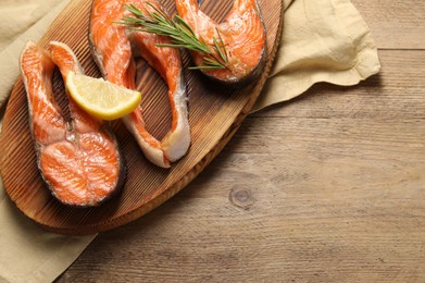 Photo of Tasty grilled salmon steaks, lemon and rosemary on wooden table, top view. Space for text